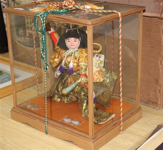 A Japanese wooden cased model of a Samurai warrior holding aloft a fan, with ornate silkwork robes, overall height 35cm, width 33cm